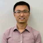 A man with black hair and glasses looks at the camera