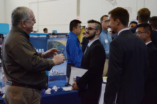 A couple students talk at a Career Fair stand with a potential employer.